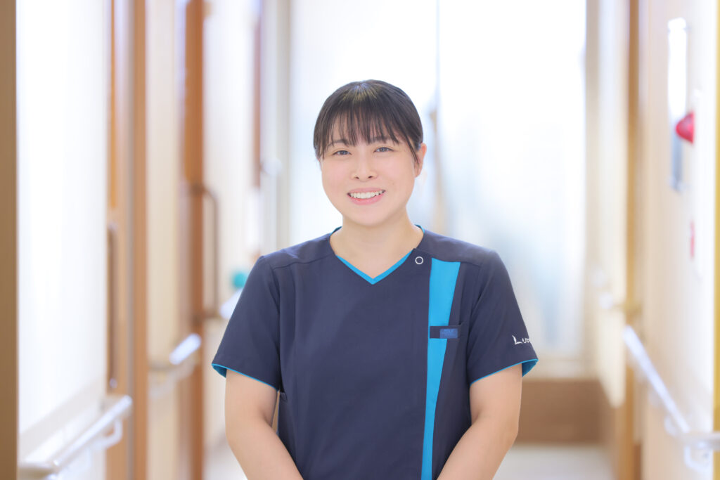 介護施設の廊下に立つ笑顔のスタッフ。白を基調とした明るい室内環境。